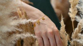 Golden charm bracelet shown on a wrist with a close up view from O. Live Love.